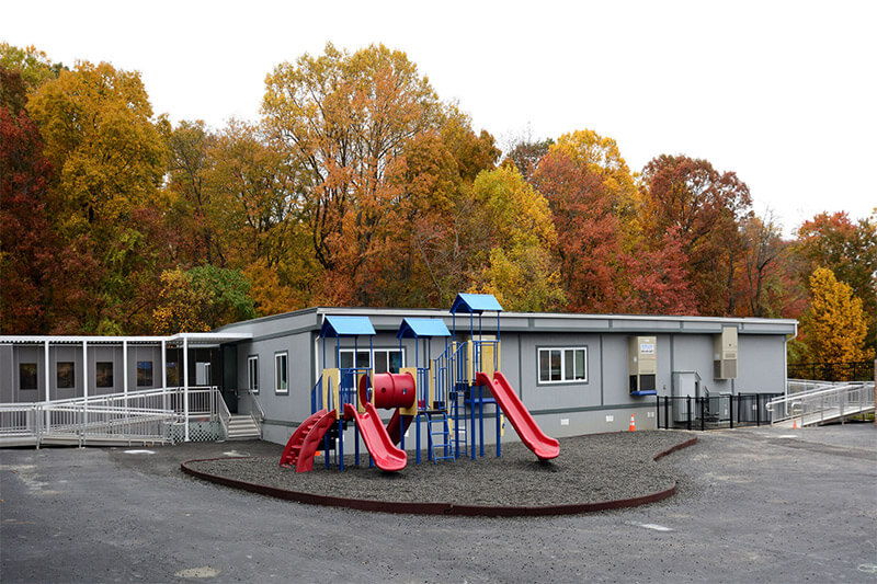 Playground with red slides in front of a gray modular classroom in Pedricktown, NJ