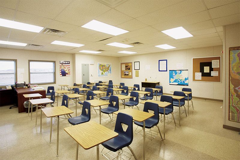 Empty modular classroom by Mobilease Modular Space with individual desks, a teacher's desk, & maps