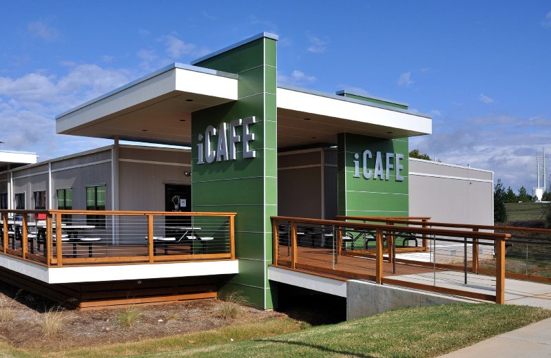 Green-colored commercial modular café building with outdoor deck, seating & modern exterior design